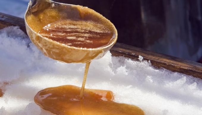A ladle drops maple syrup on snow